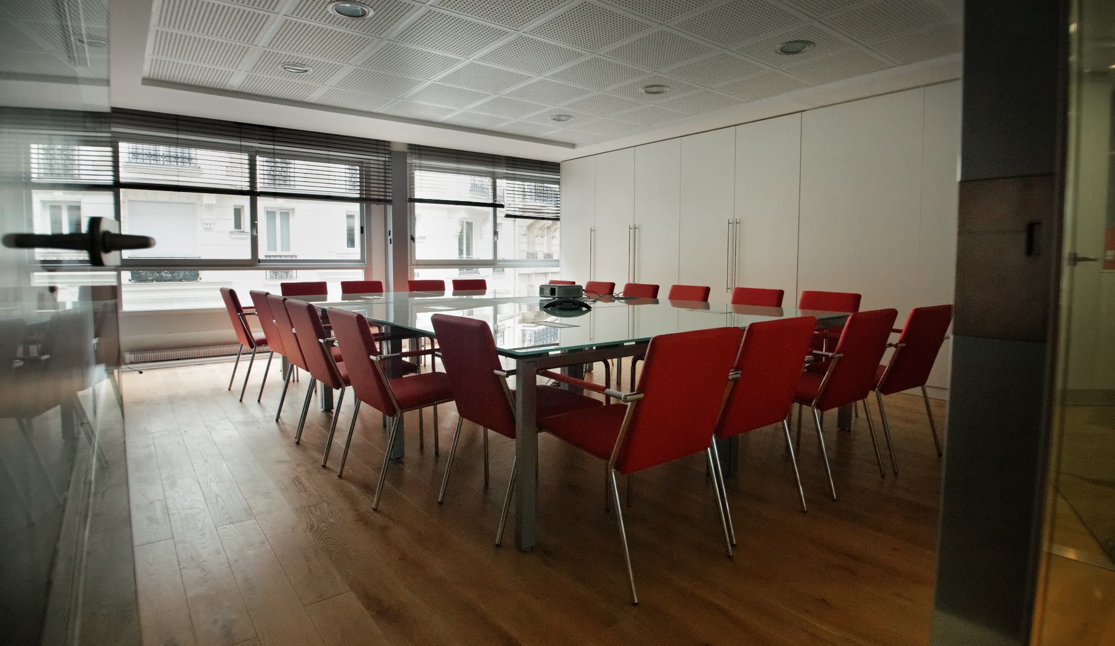 Salle de réunion CGE, table en verre et sièges rouges.
